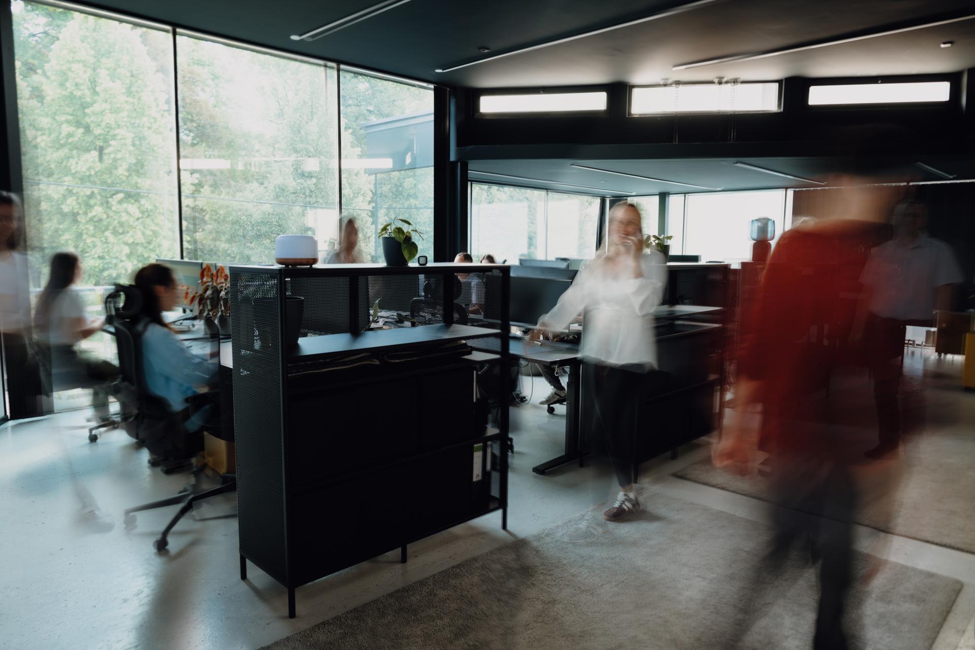 Busy open-plan office with floor-to-ceiling windows and a view of trees