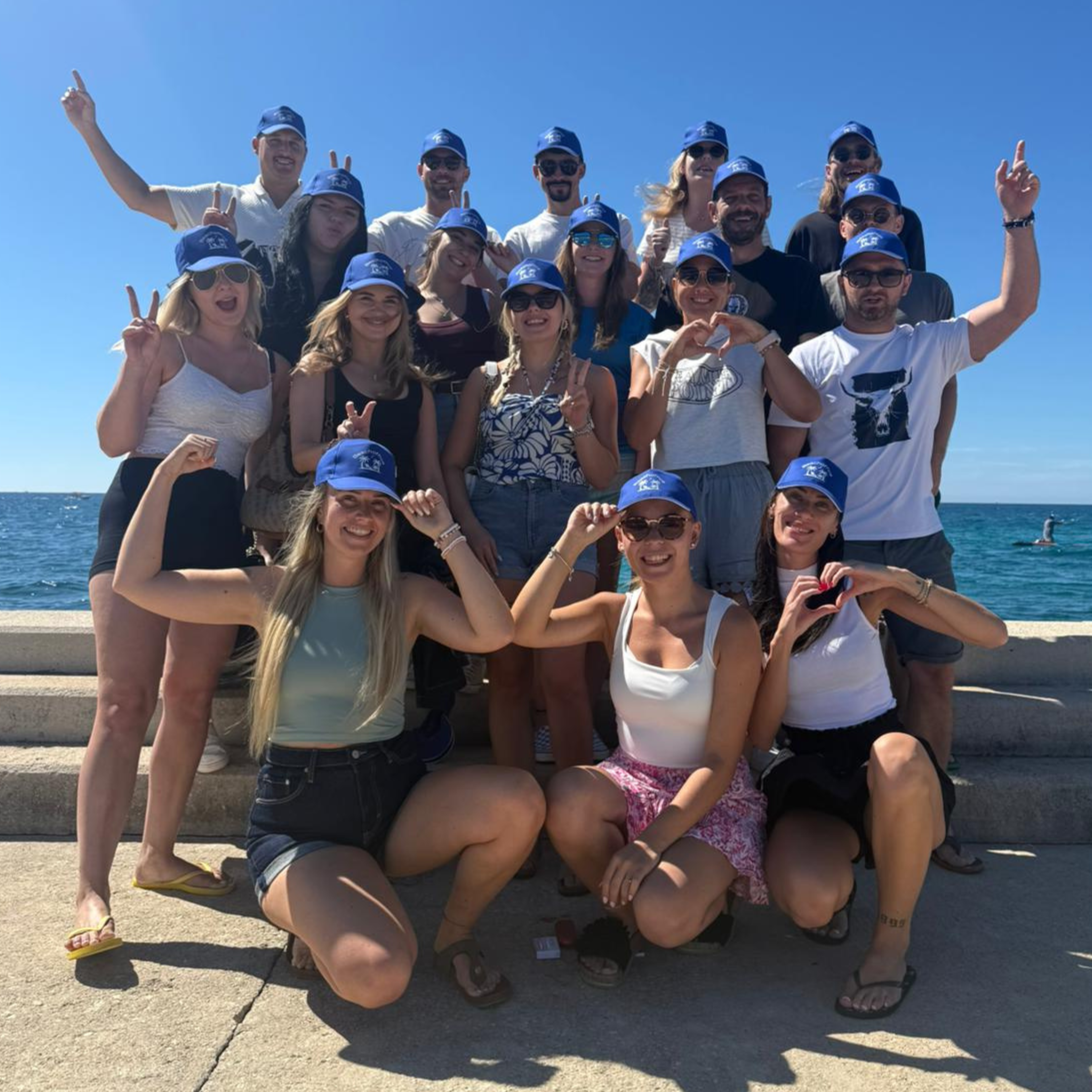 The team posing together by the sea in matching blue caps