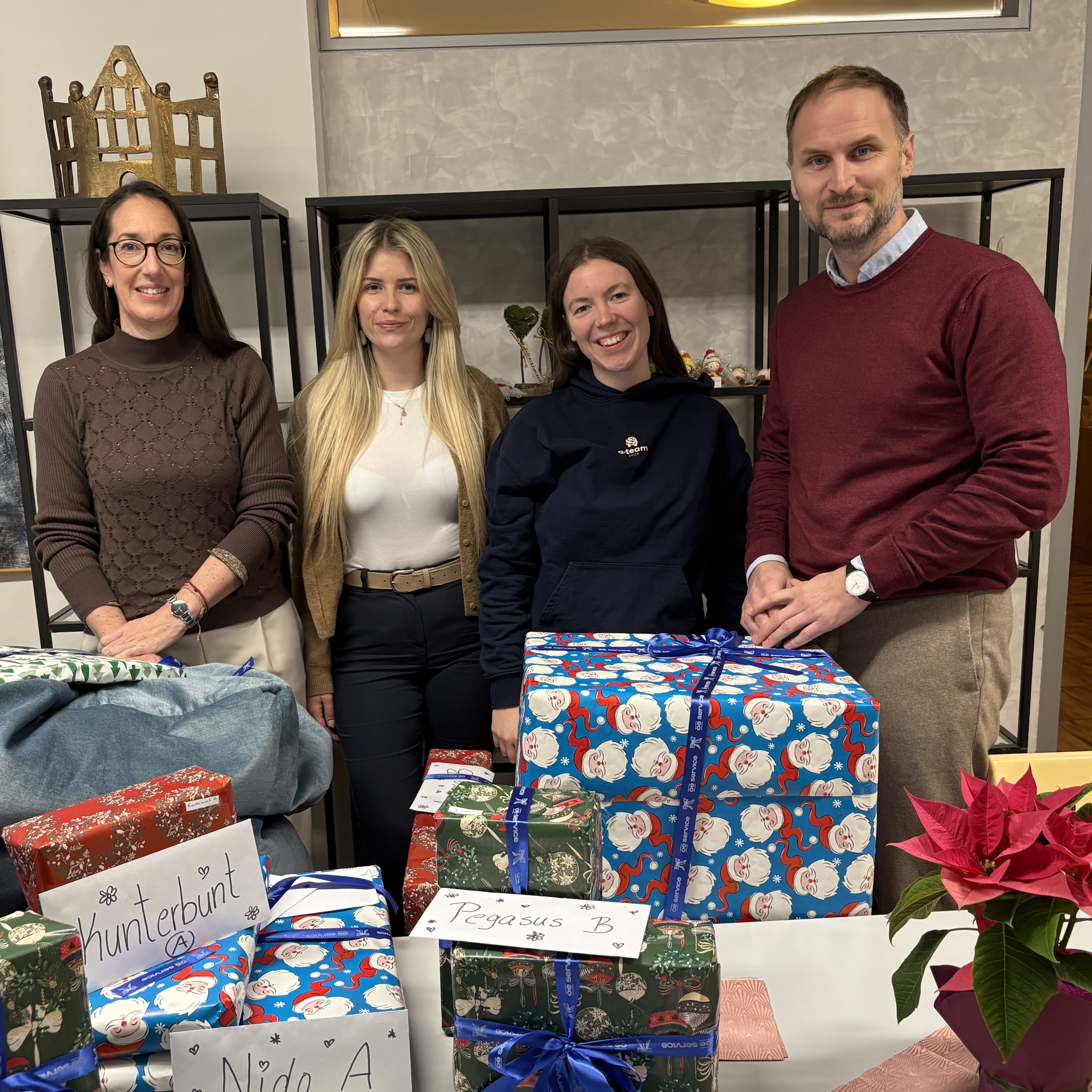 Four team members standing behind a table of wrapped Christmas gifts